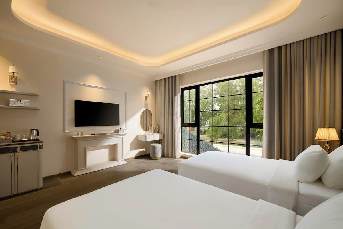 A hotel room with two beds, a TV, a minibar, and a large window with curtains.