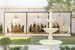 A covered outdoor dining area with a tiered fountain, a stone pathway, and neatly arranged wooden tables and chairs. - Narci Resort Tam Coc (Hoa Lu)
