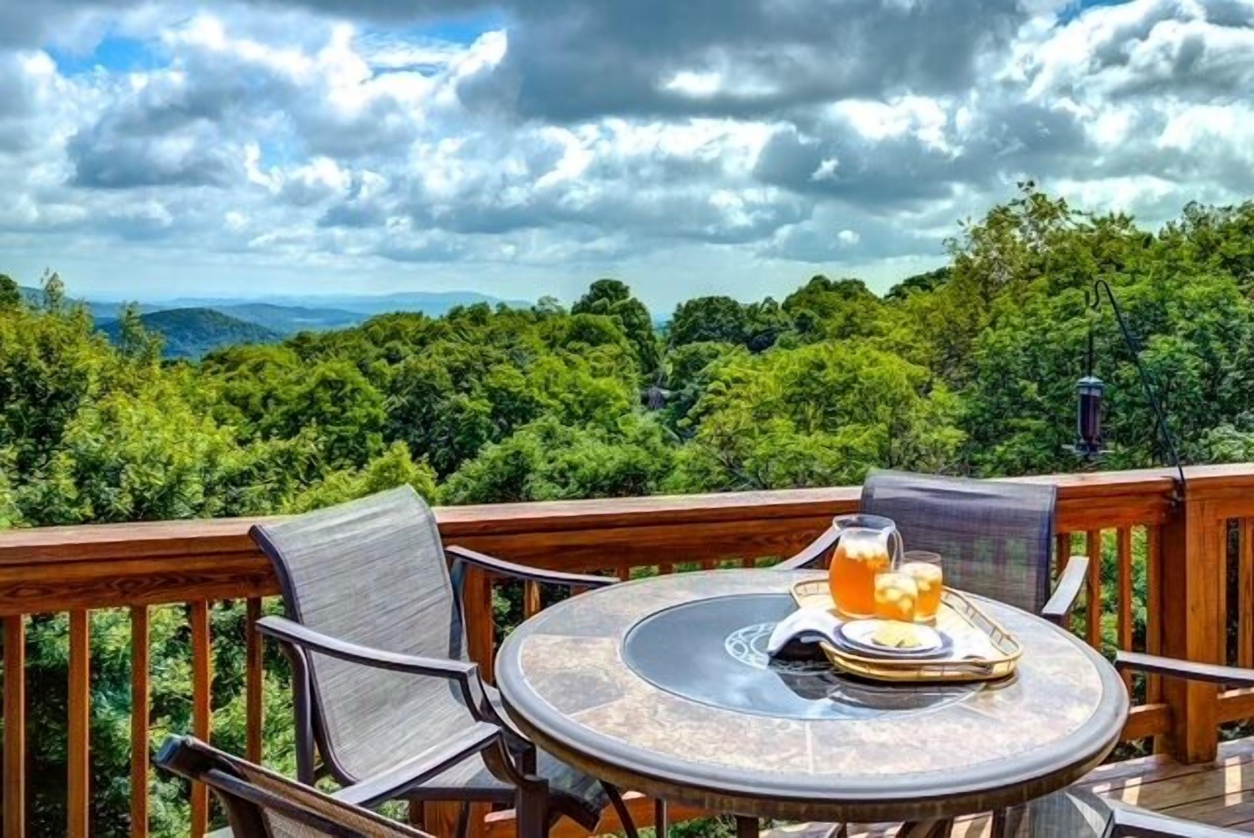 A round table with chairs on a deck, overlooking a forested landscape.