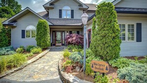 Una casa de dos pisos con un camino de piedra que conduce a la puerta principal, rodeada de arbustos y un cartel que dice 'Blue Spruce Overlook'.