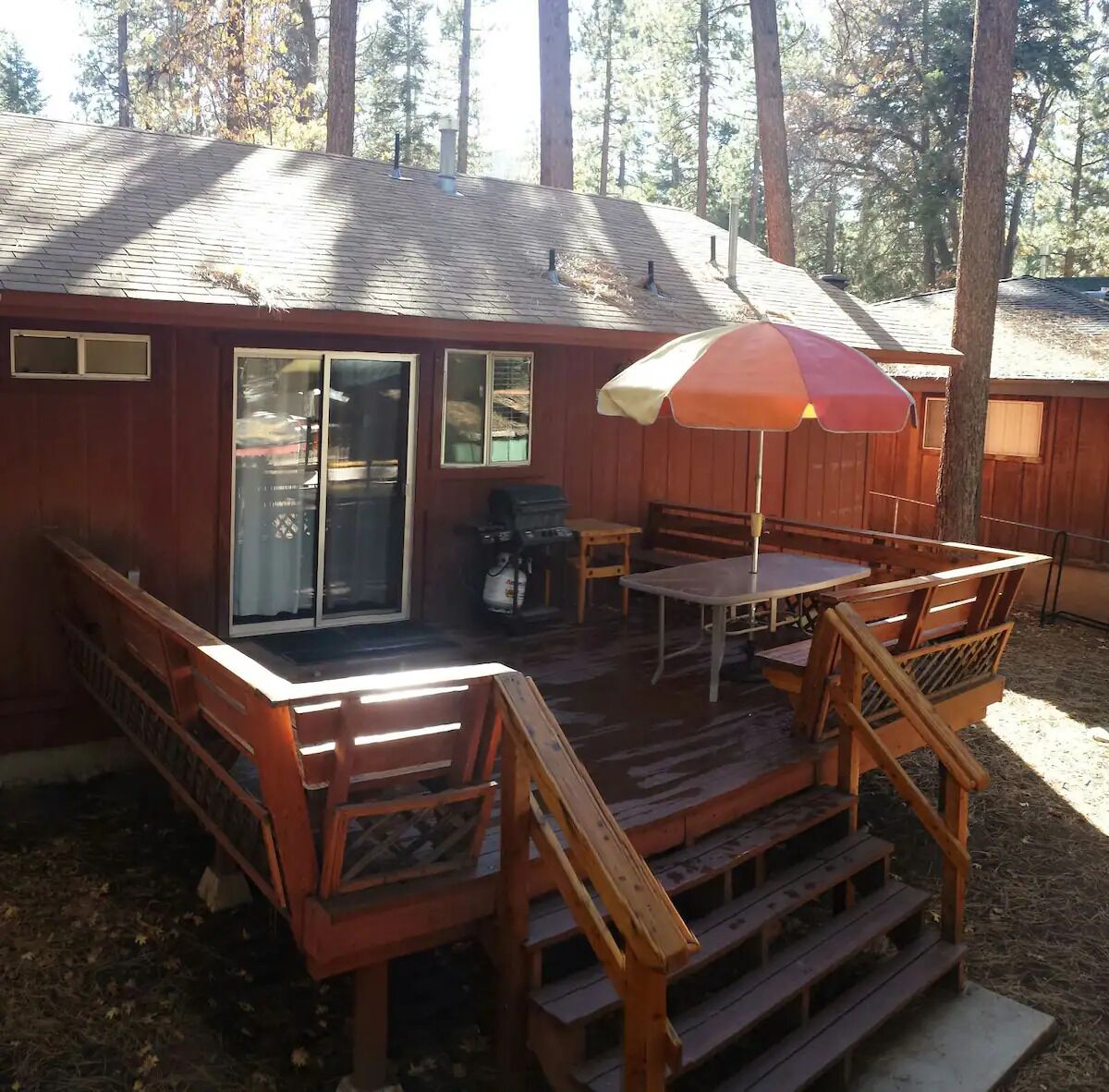 Une terrasse en bois avec une table et des chaises, un barbecue et un espace patio couvert.