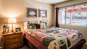 A bedroom with a large bed, a nightstand with a lamp, a dresser, and two framed pictures on the wall. - Cozy 2-BR/2-BA cabin in Big Bear perfect for a relaxing, close to the slopes (Big Bear Lake)