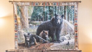 A living room with a sofa, two patterned cushions, a coffee table with a foosball table, and a tapestry of a bear in a forest. - Cozy 2-BR/2-BA cabin in Big Bear perfect for a relaxing, close to the slopes (Big Bear Lake)