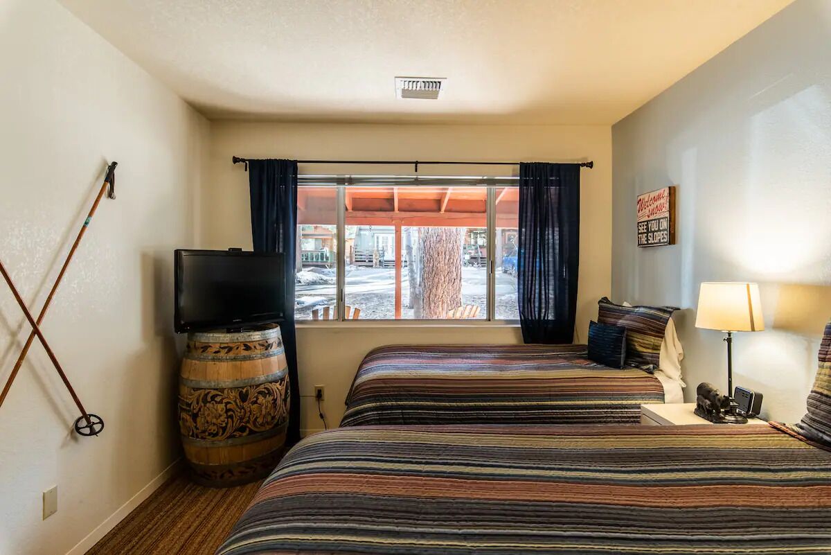 Habitación de hotel con dos camas, televisión, una mesita y ventana con cortinas.