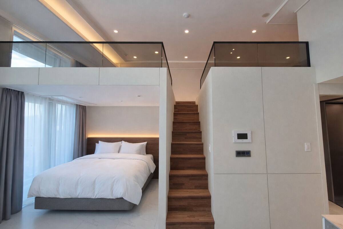 Un dormitorio moderno con una cama grande, una escalera de madera y un balcón de vidrio.
