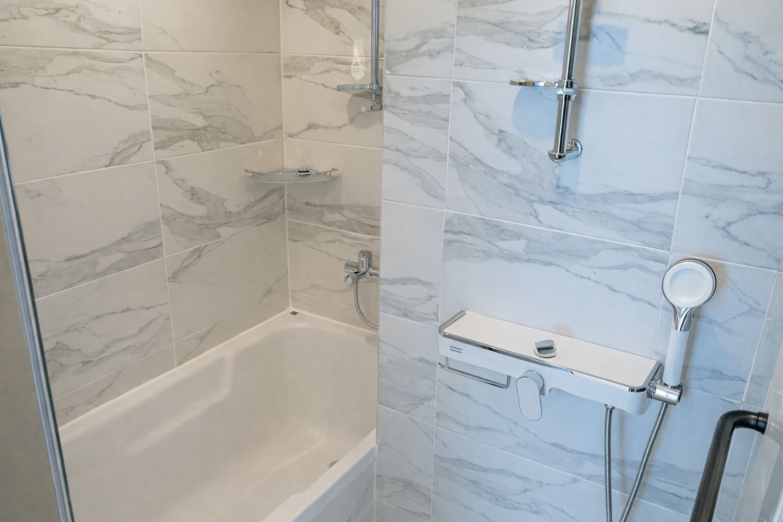 A bathroom with a bathtub, a shower with a handheld showerhead, and a glass shelf.