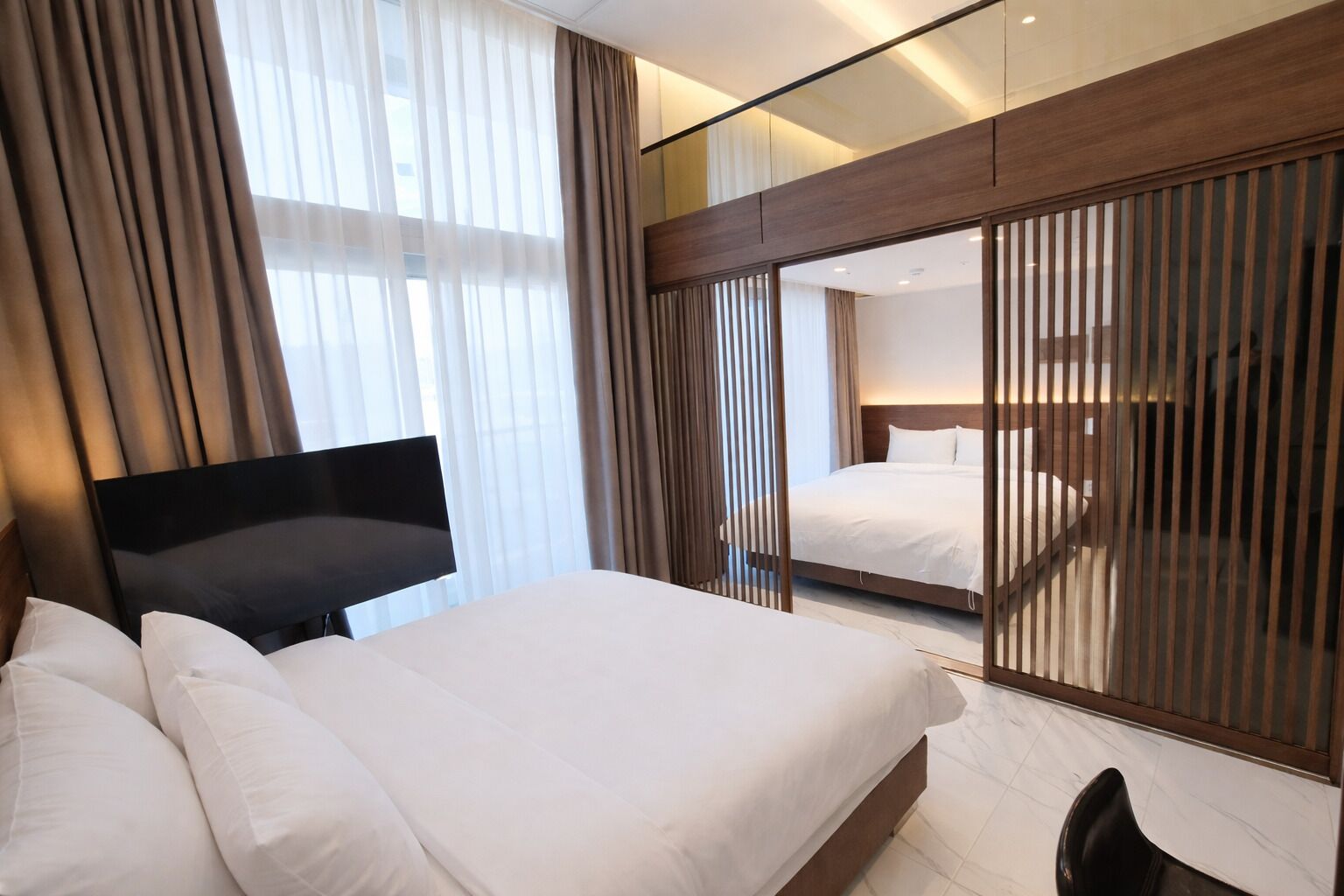 A modern hotel room with a large bed, a flat-screen TV, and a sliding door closet.