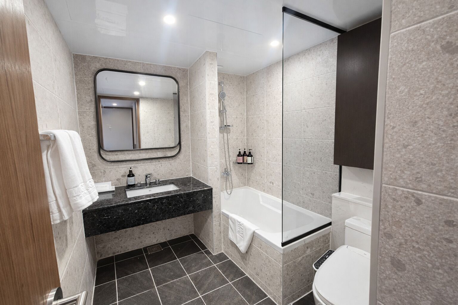 Un baño moderno con lavamanos de mármol negro, un espejo grande, una bañera y un inodoro.