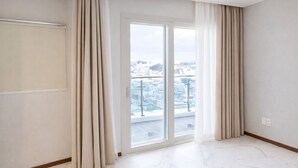 Une pièce spacieuse dotée d’une grande porte-fenêtre coulissante donnant sur un balcon avec vue sur la ville.