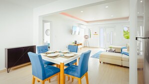 Una sala de estar moderna con comedor, sofá, televisor y área de cocina.