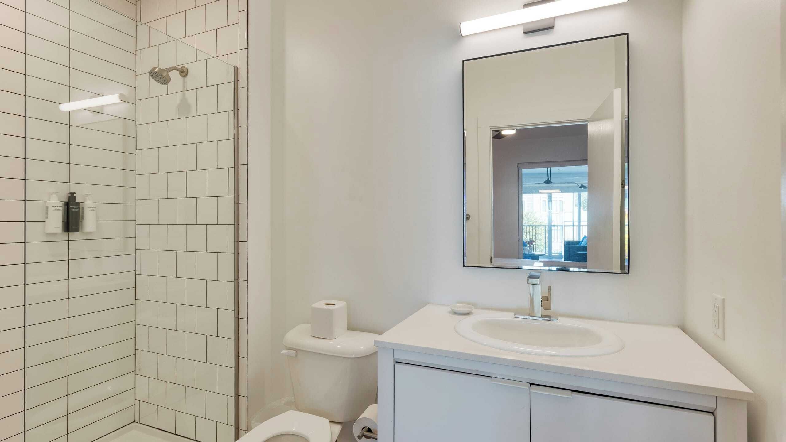 A modern bathroom with a glass shower enclosure, a white sink with a mirror above it, and a toilet with a roll of toilet paper.