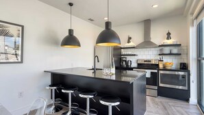 Una cucina moderna con isola centrale, sgabelli da bar, illuminazione a sospensione ed elettrodomestici in acciaio inossidabile.
