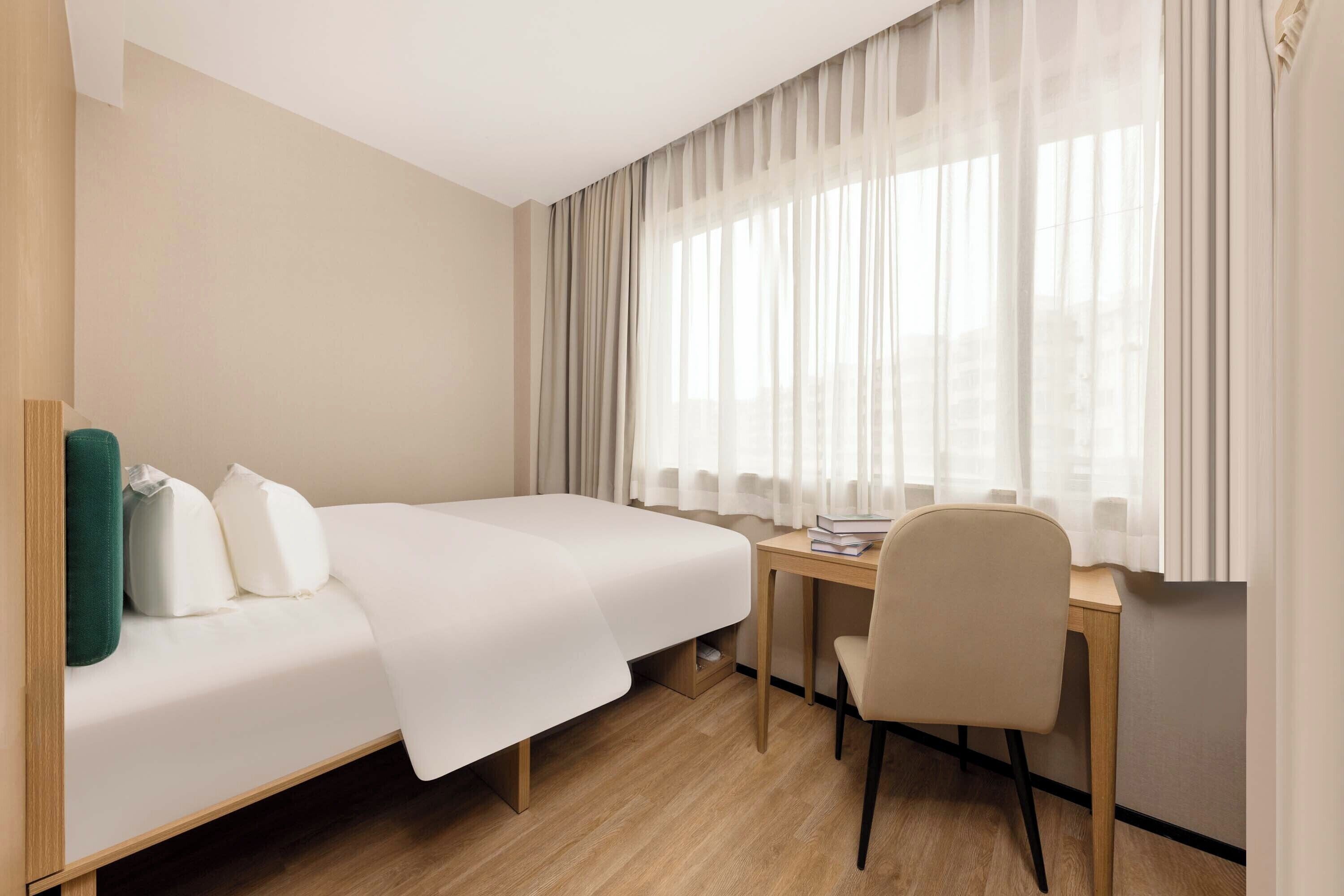 A hotel room with a bed, a desk, a chair, and a window with curtains.