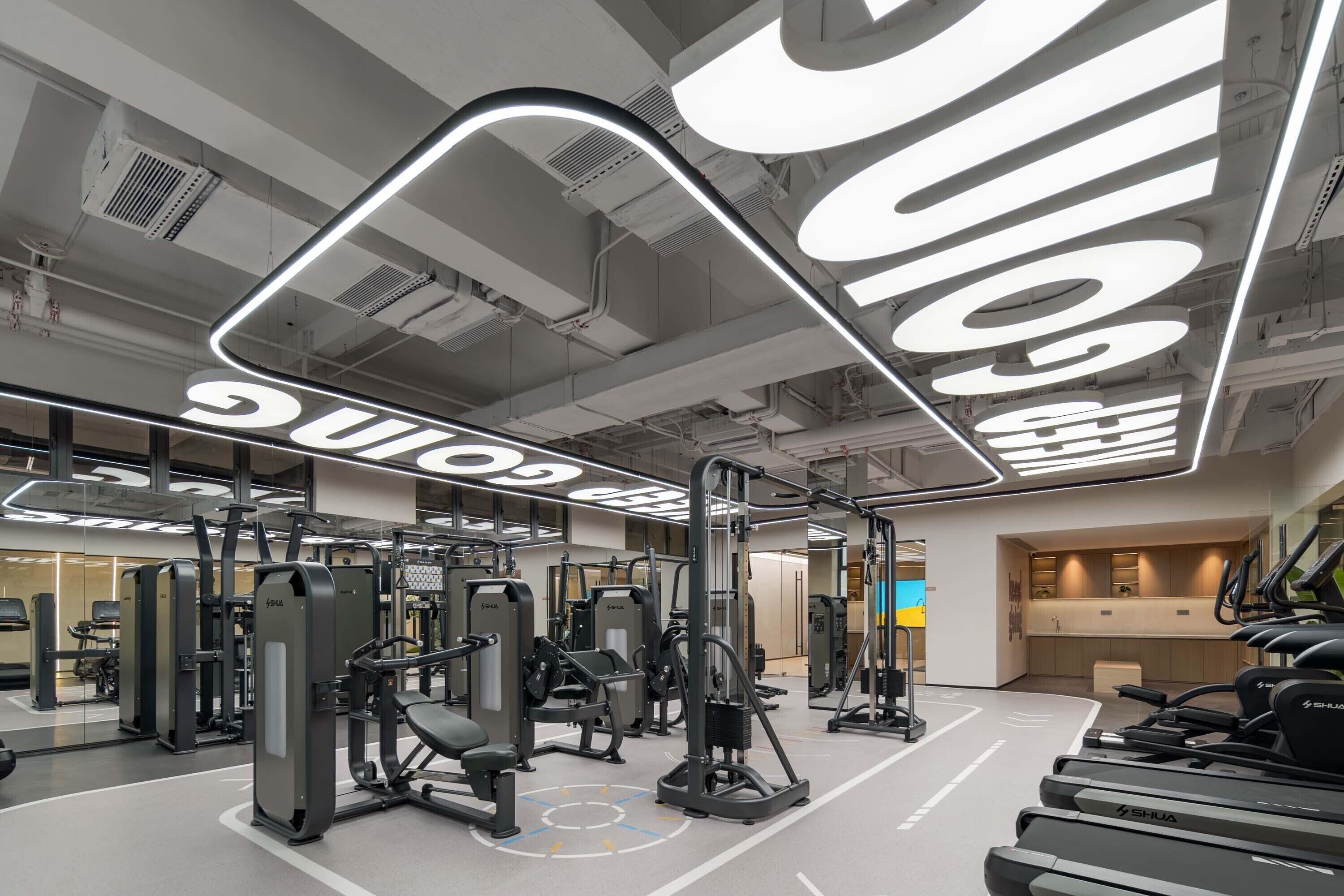 A modern gym with various exercise equipment, a reception area, and a large illuminated sign.