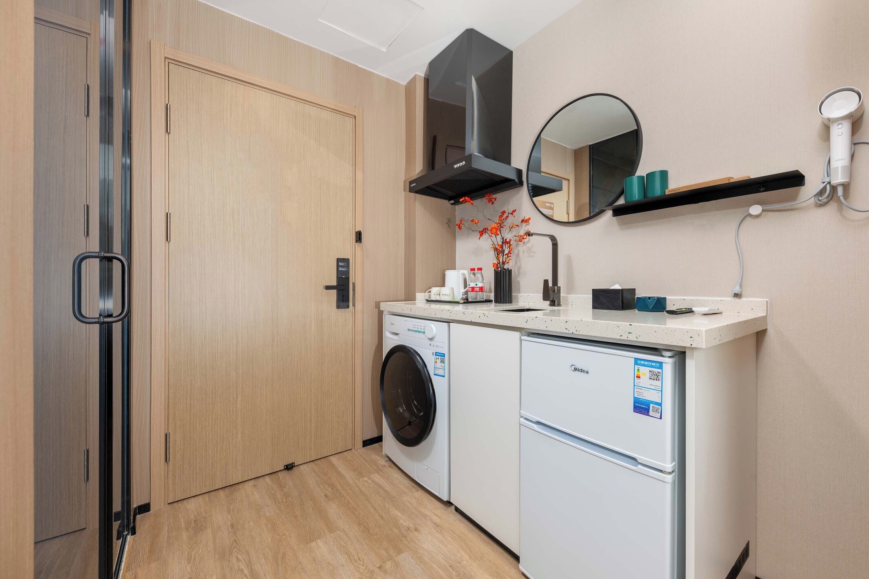 Een kleine hotelkamer met een wasmachine, een kleine koelkast, een magnetron, een spoelbak en een spiegel.