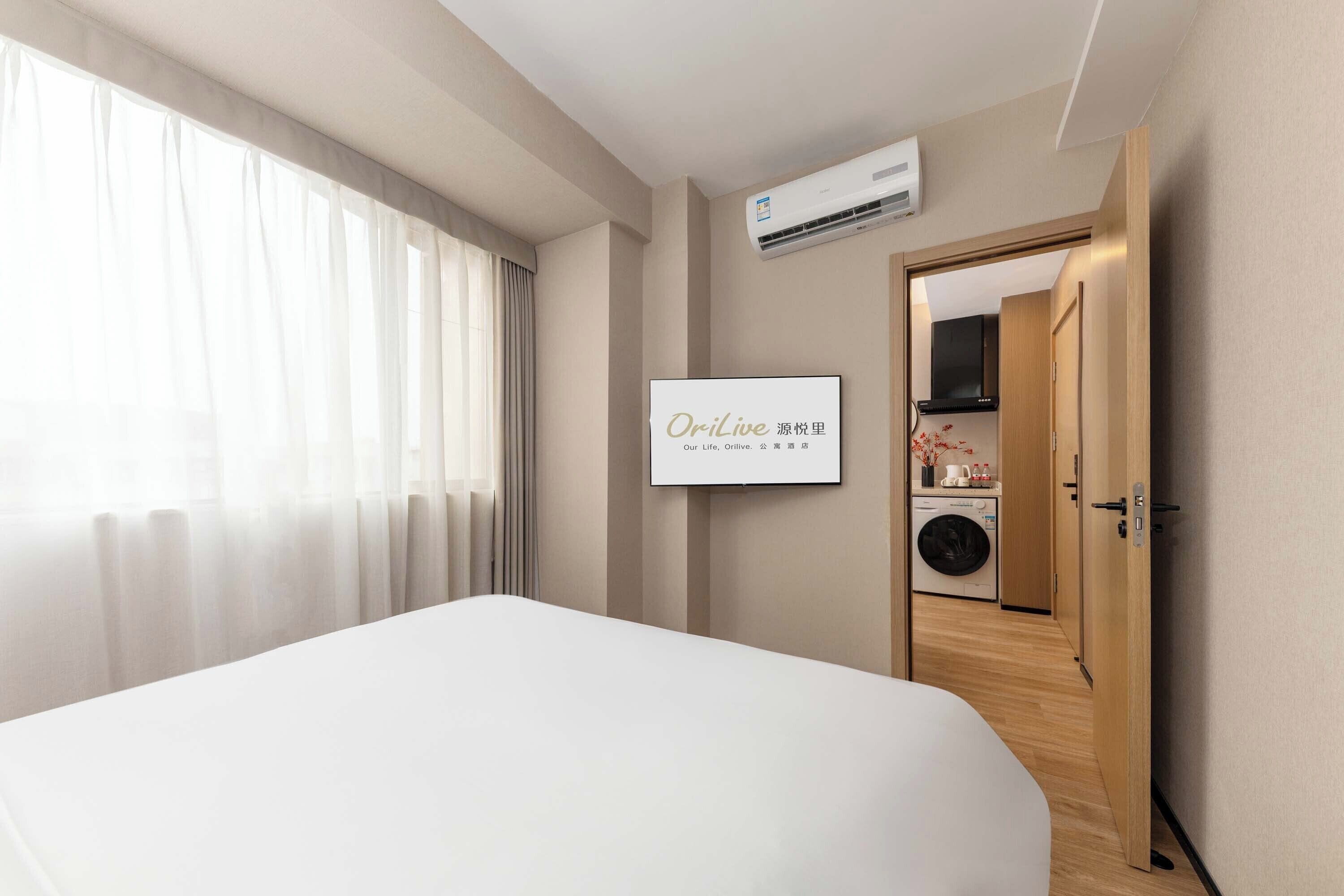 A hotel room with a bed, an air conditioning unit, a framed sign, a washing machine, and a wooden door.