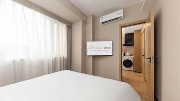 A hotel room with a bed, an air conditioning unit, a framed sign, a washing machine, and a wooden door.