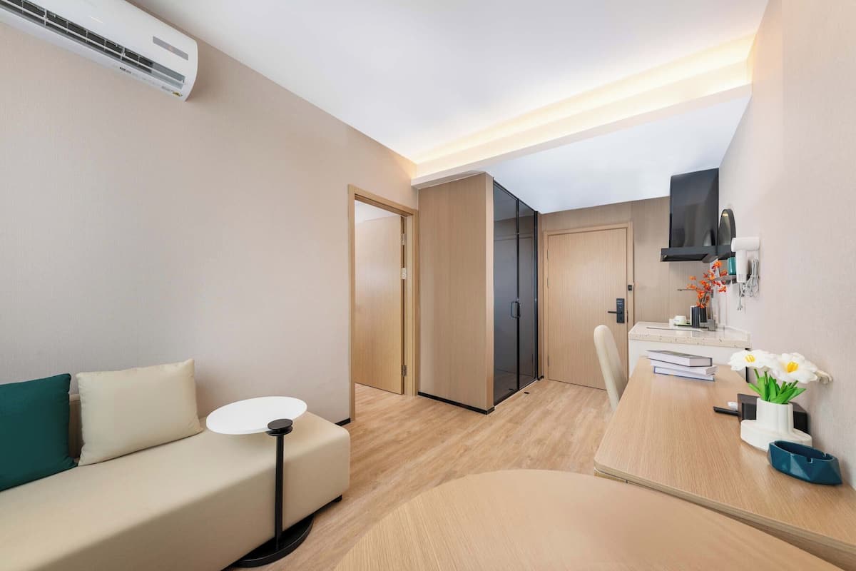 Een moderne hotelkamer met een bank, een klein rond tafeltje, een bureau met stoel, een spiegel en een aan de muur bevestigde televisie.