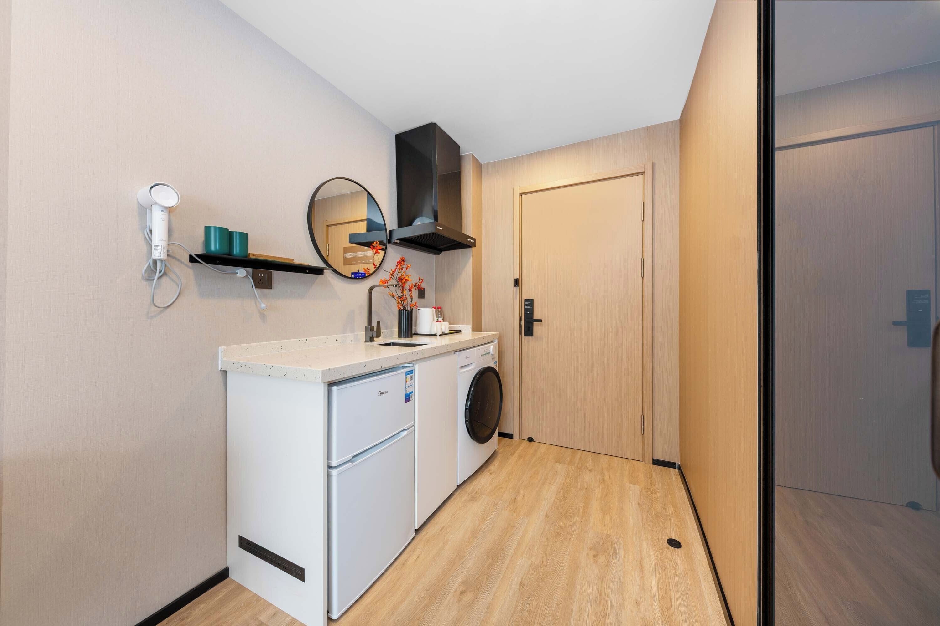 A compact kitchenette with a washing machine, a small refrigerator, a microwave, and a coffee maker.