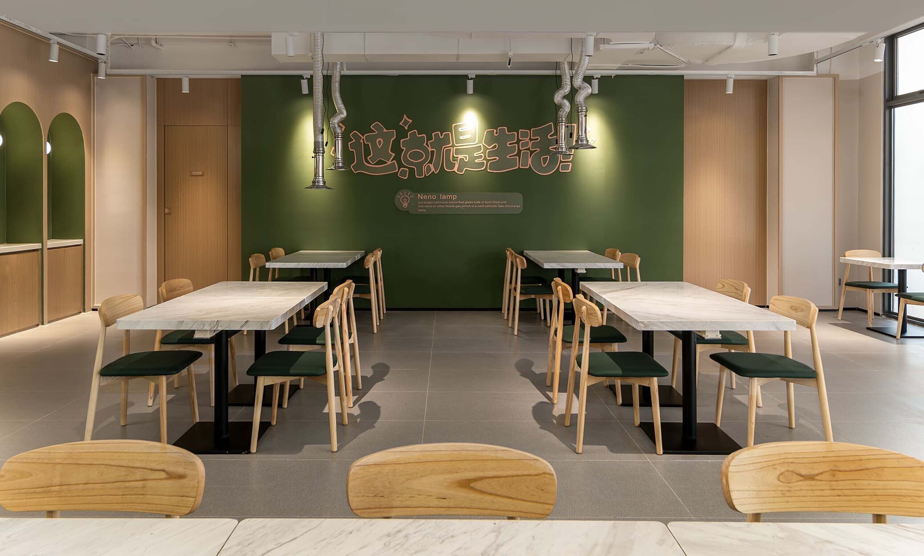 A conference room with multiple tables and chairs, a green accent wall with text, and a ceiling with ventilation ducts.