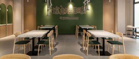 A conference room with multiple tables and chairs, a green accent wall with text, and a ceiling with ventilation ducts.