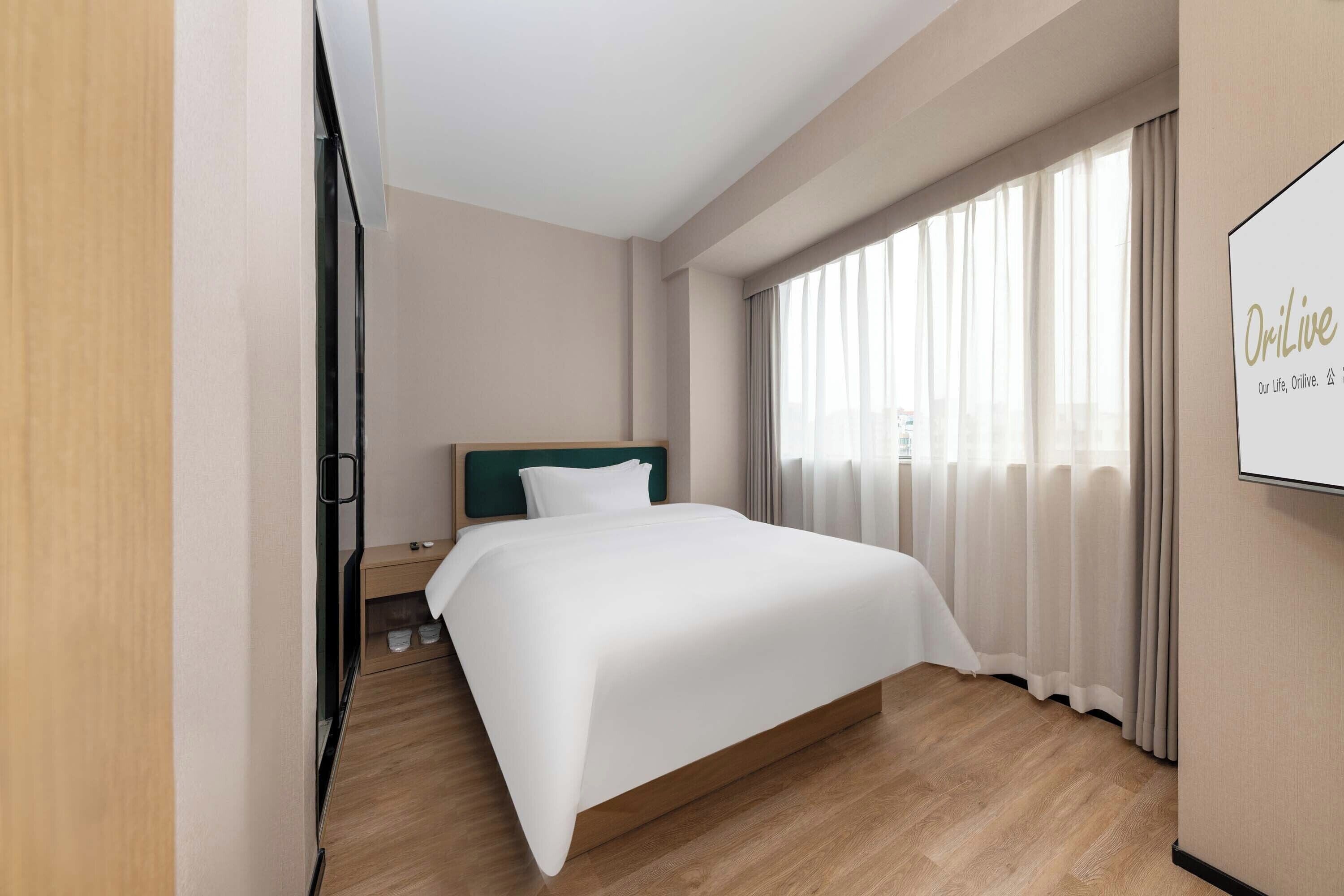 Une chambre d’hôtel avec un grand lit, une table de chevet, un miroir et une fenêtre avec des rideaux.