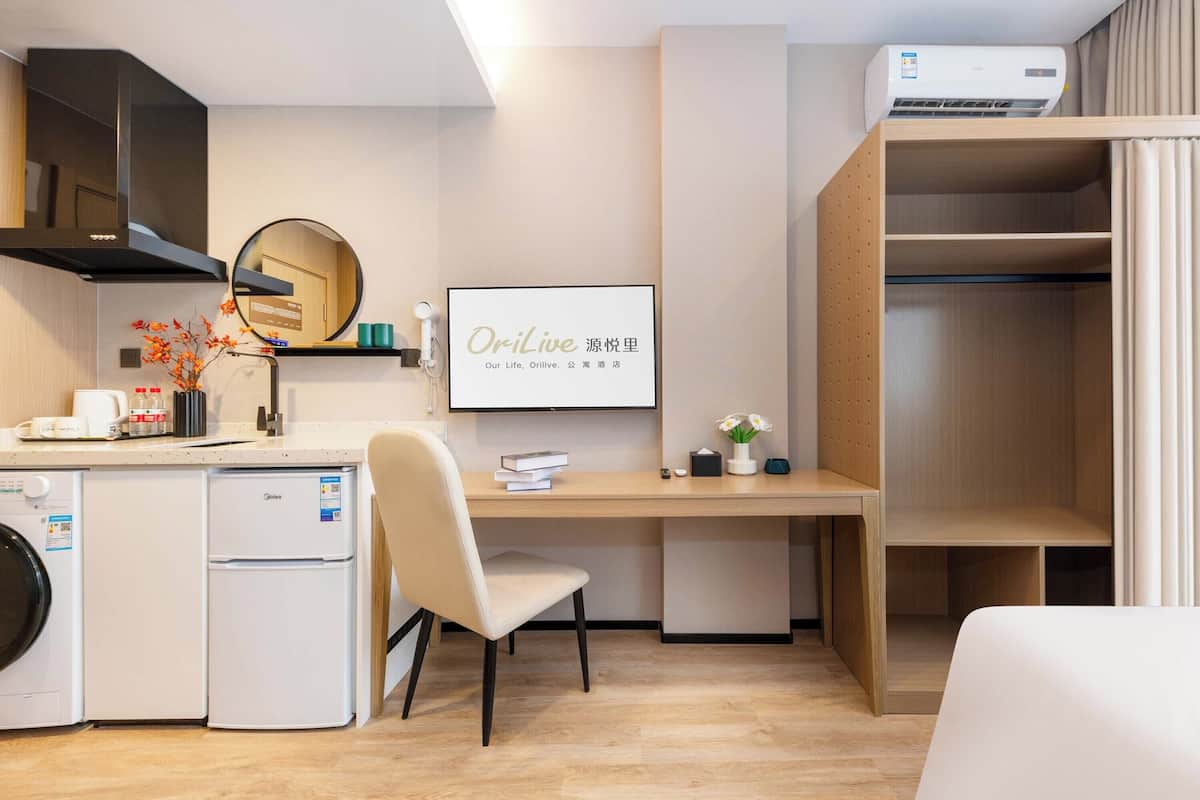 Een moderne hotelkamer met kitchenette, bureau, stoel, kledingkast en bed.