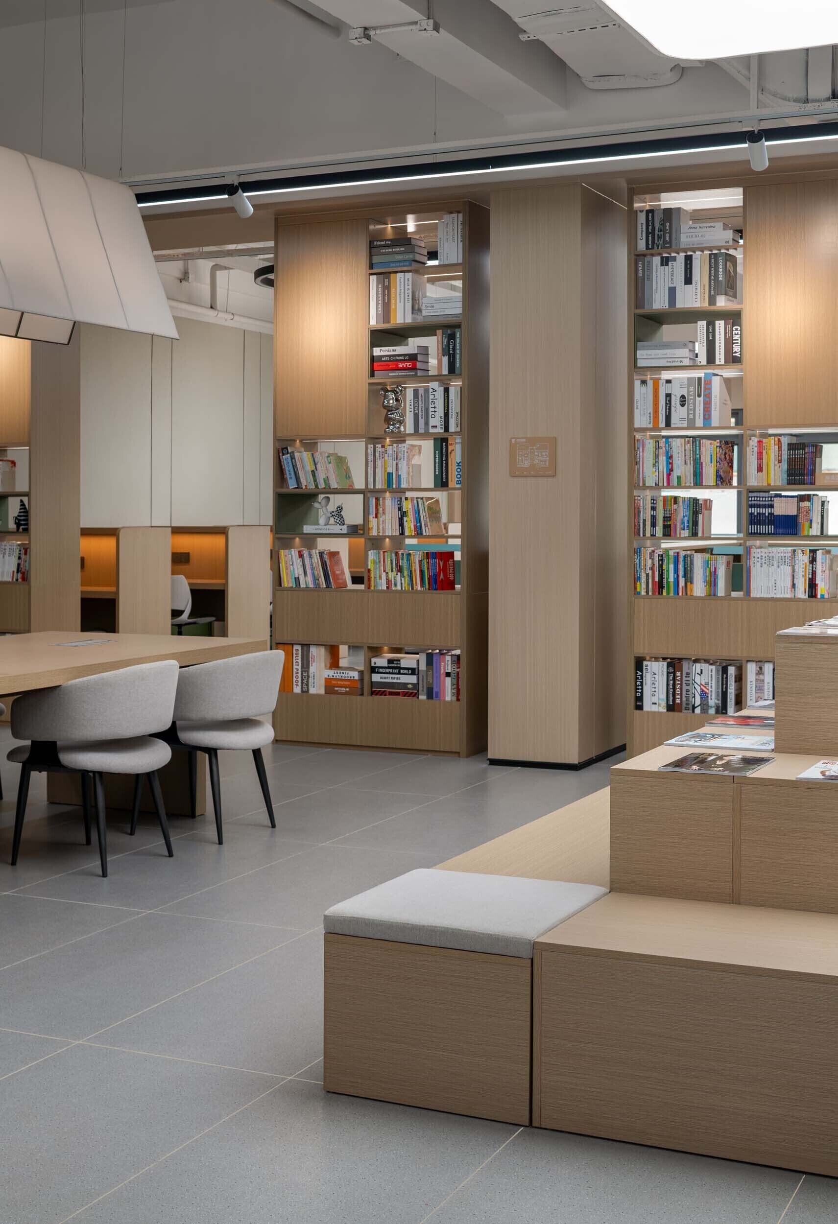 Una biblioteca moderna con estanterías de madera, una zona de estar con sillas y una mesa.