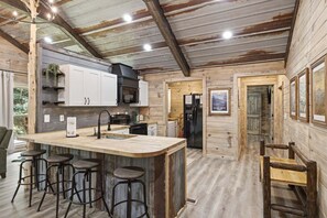 A rustic kitchen with a central island, bar stools, and a black refrigerator. - Rustic Retreat — Easy Access, Peaceful Setting, Close to Everything (Sevierville)