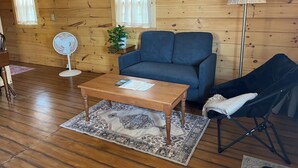 Een houten cabin interieur met een bank, een kleine tafel, een lamp, een ventilator en een potplant.