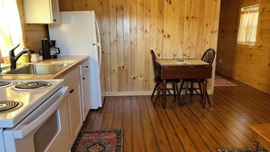 Een kleine keuken met houten wanden, een witte koelkast, een fornuis en een eettafel met stoelen.