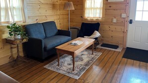 Interieur van een houten hutje met een bank, een tafel, een stoel, een lamp en een potplant.