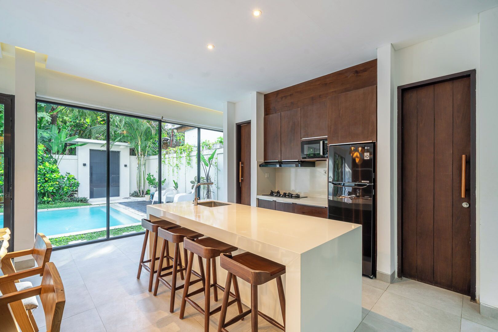 Una cocina moderna con una isla grande, taburetes de bar, horno empotrado y vistas a una piscina.