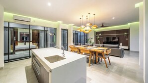 Une cuisine moderne dotée d’un îlot central, un coin repas avec des meubles en bois et un espace de vie comprenant un canapé et un téléviseur.