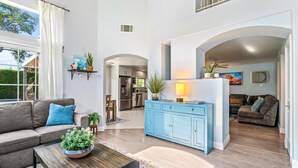 A spacious living area with a grey sofa, a blue cabinet, and a dining table with a plant.