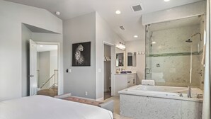 A modern bedroom with a large bed, a walk-in closet, a bathroom with a glass shower, and a marble vanity.