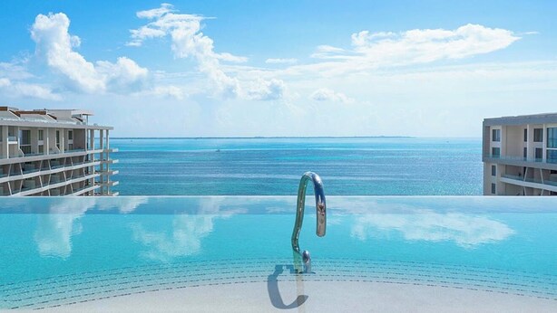 Une piscine à débordement offrant une vue dégagée sur l’océan, avec un bâtiment situé sur la gauche.