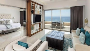 Une chambre d’hôtel moderne équipée d’un lit, d’une télévision, d’un balcon avec vue sur la mer et d’un coin salon avec une table basse.