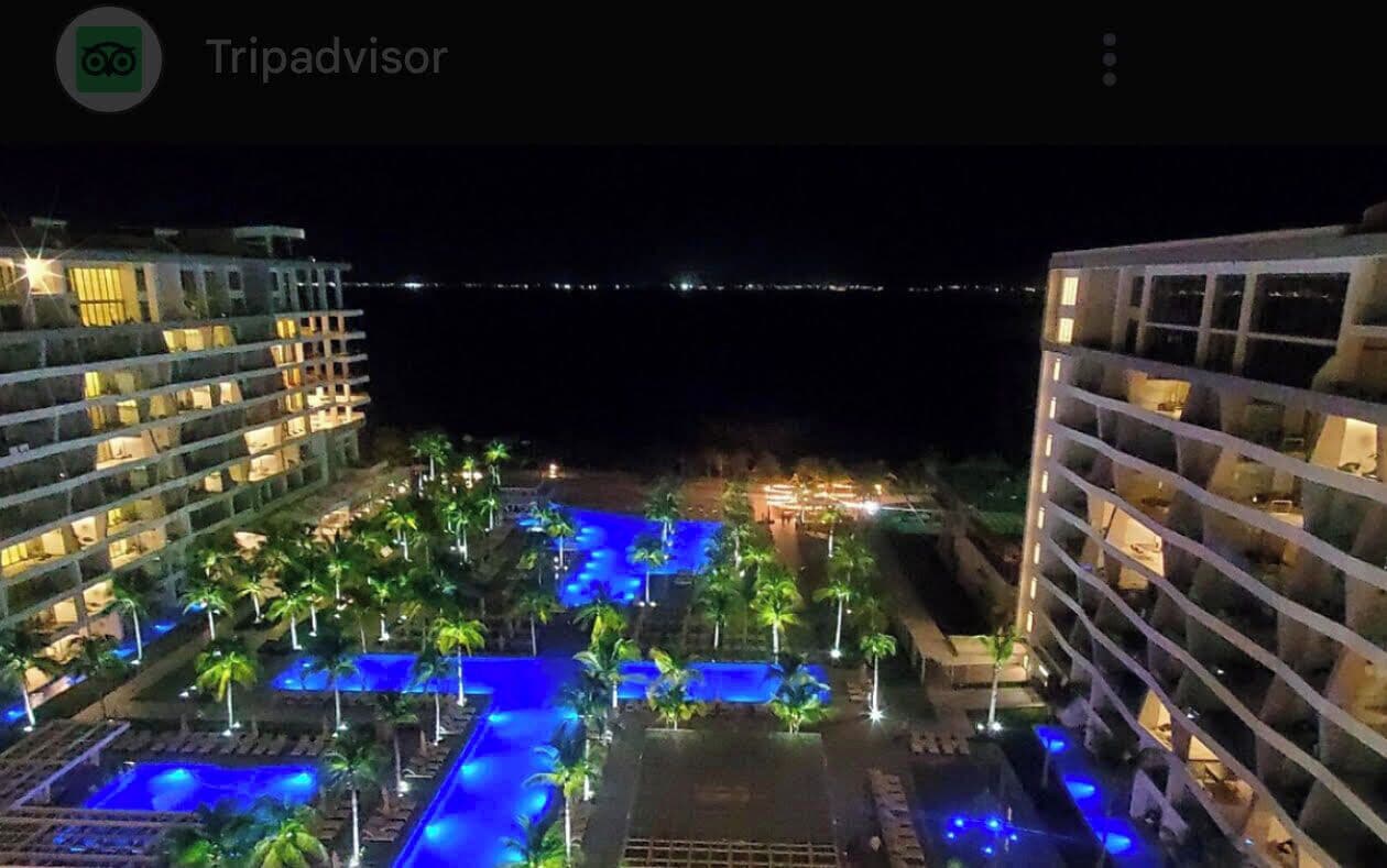 A nighttime view of a hotel with multiple swimming pools and palm trees, illuminated by blue lighting.