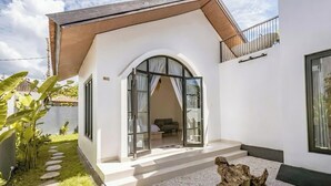 Une maison moderne avec une façade blanche, un toit en bois et une porte en verre donnant sur un intérieur comprenant un canapé et une table.