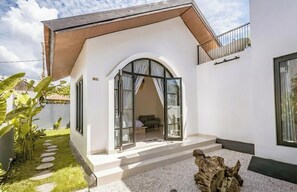 Una casa moderna con fachada blanca, techo de madera y puerta de cristal que da a un interior con sofá y mesa.