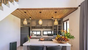 Une cuisine moderne dotée d’un îlot central, de luminaires suspendus et d’un panier à fruits.