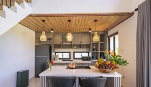 A modern kitchen with a central island, pendant lighting, and a fruit bowl. - Algera Villa Ubud (Mas)