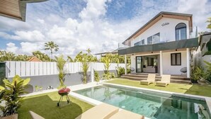 Une maison moderne dotée d’une piscine, d’un barbecue et d’un patio couvert.