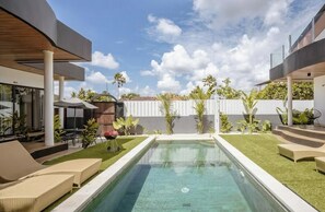 Uma área moderna com piscina ao ar livre, cadeiras de espreguiçadeira, churrasqueira e área de estar coberta.