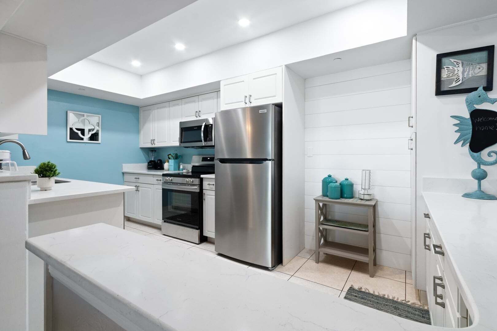 Una cocina moderna con armarios blancos, electrodomésticos de acero inoxidable y una pared de acento azul.