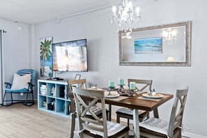 A dining area with a wooden table, chairs, candles, and a TV on the wall. - Sandpiper Towers 408 (Satellite Beach)