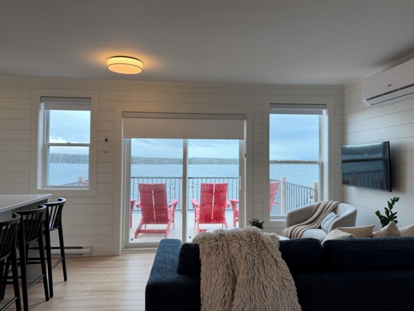 A living room with a sofa, chairs, a television, and a view of the water. - Saltwater Steeple- Bell Tower Suite (Port Saunders)