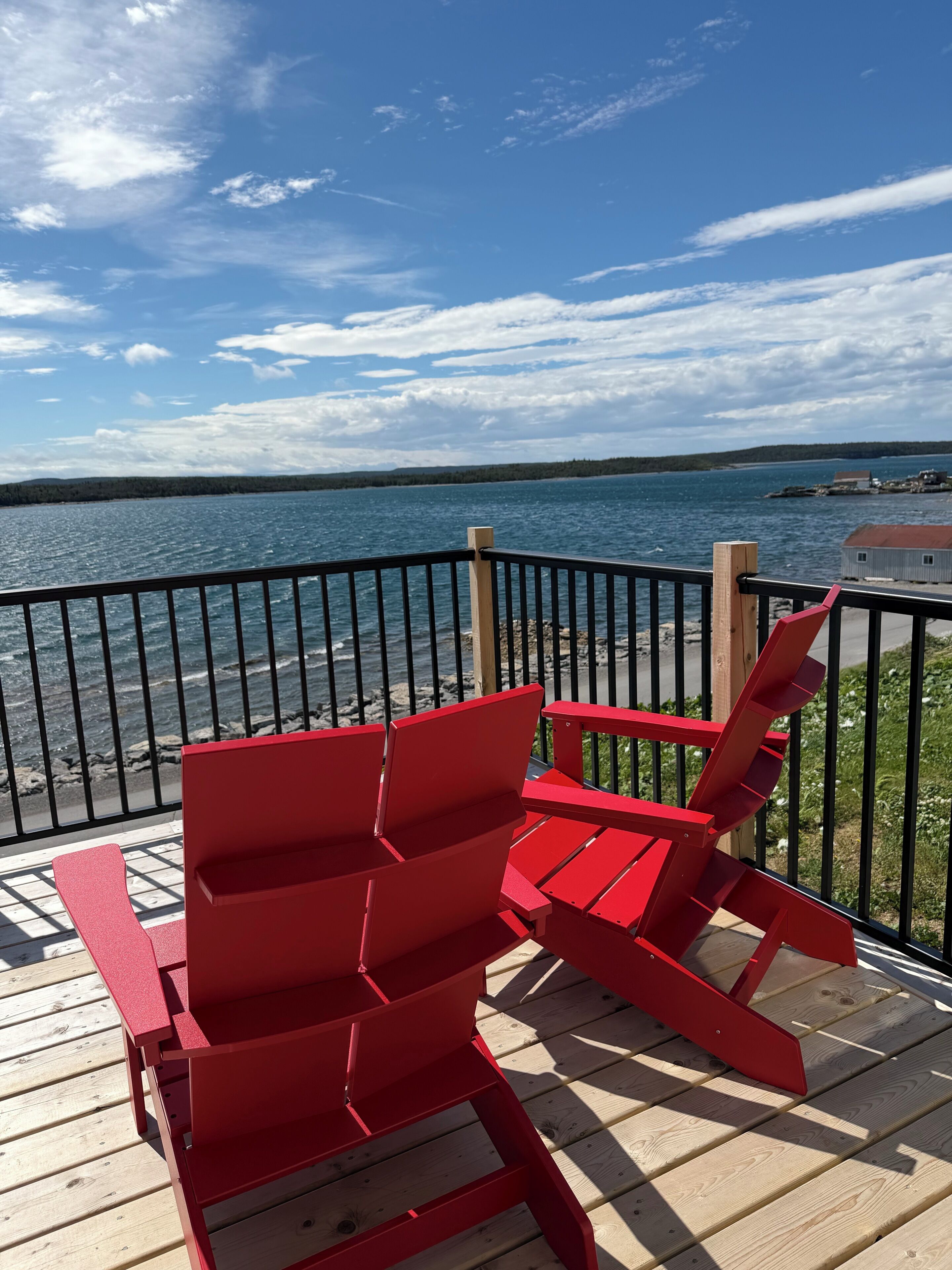 A deck with red Adirondack chairs overlooking a body of water.