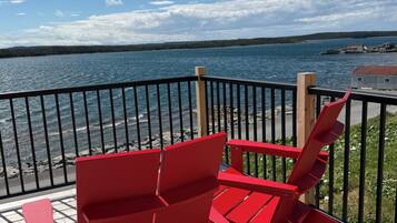 A deck with red Adirondack chairs overlooking a body of water.